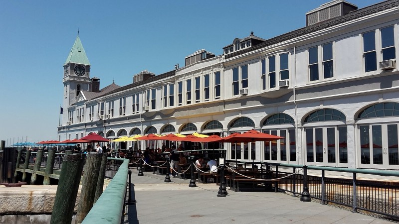 Pier A Harbor House open on a sunny day in June 2016, red and yellow umbrellas over full tables on the plaza and the clock tower above