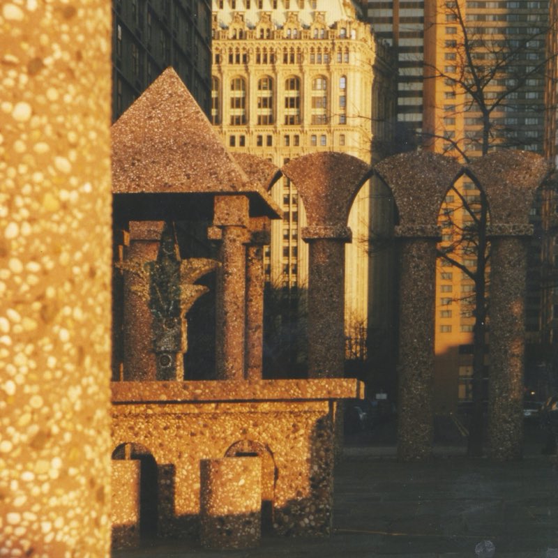 The Upper Room in low winter sun in December 1998: its pebbled concrete pyramid, columns and arcade glowing orange, an old office tower behind